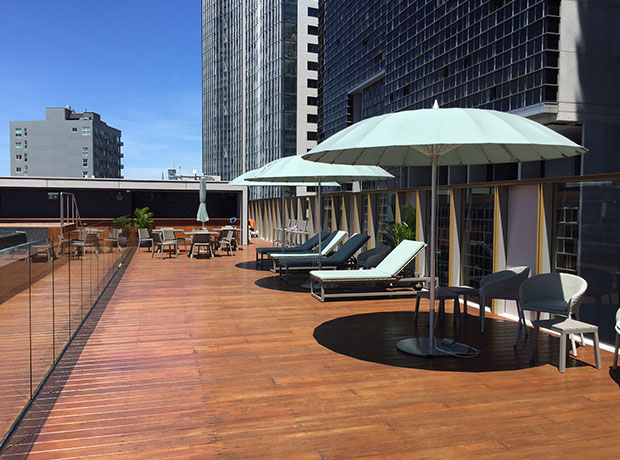 The Old Clare Rooftop lounges near bar and lap pool. High-rise neighbouring buildings. 

