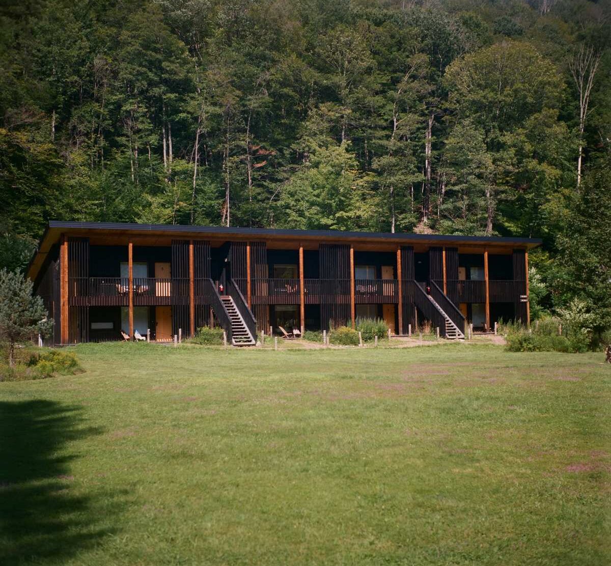 Eastwind Oliverea Valley A clear view of the valley guest rooms: dark timber, private entrances and terraces opening directly onto an enormous green lawn—an especially forgiving setup when traveling with a child and a dog