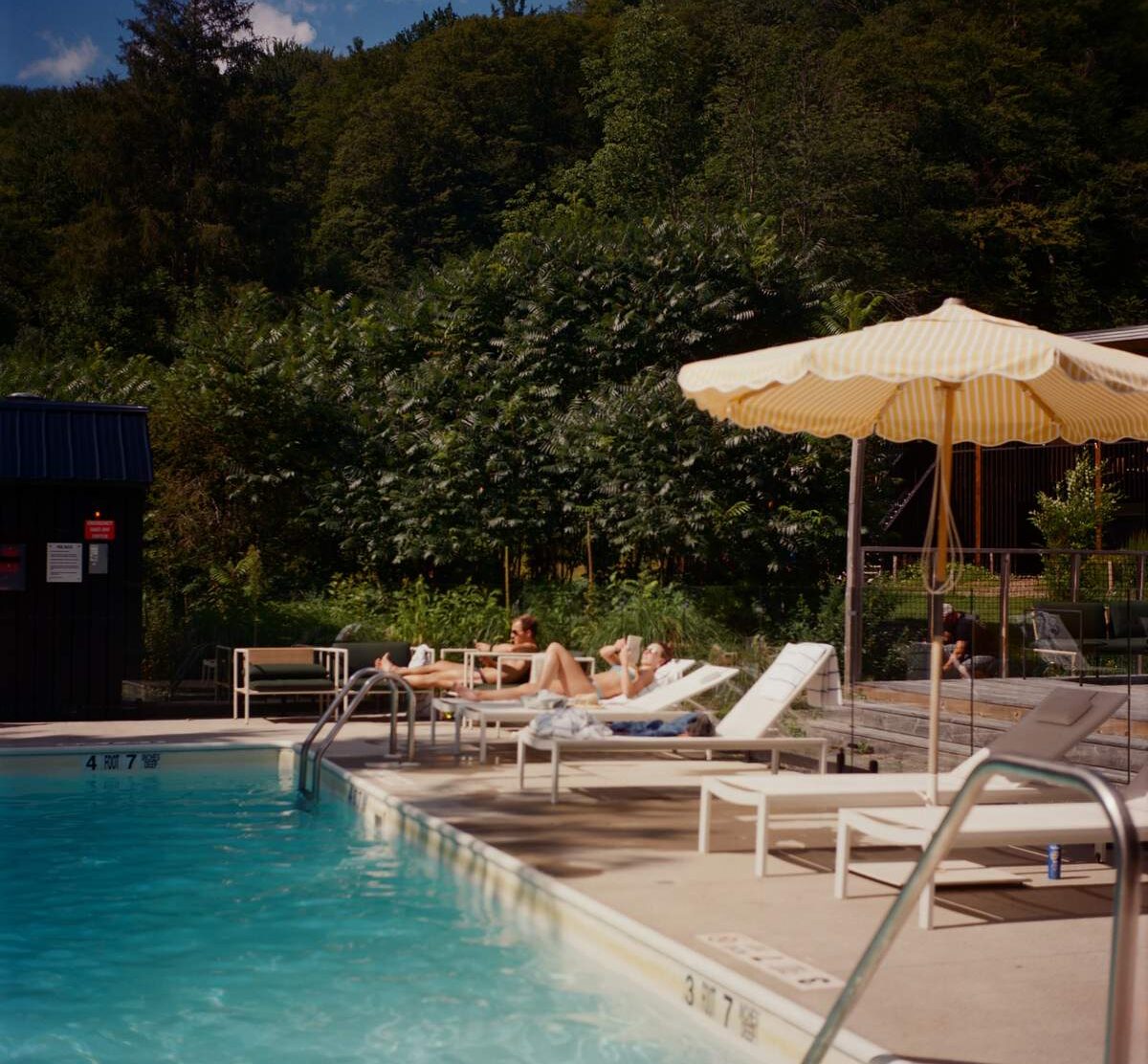 Eastwind Oliverea Valley The heated pool in full summer mode: pale loungers, a yellow-striped umbrella and dense green Catskills foliage. It feels social when families gather, then almost meditative once the water goes still